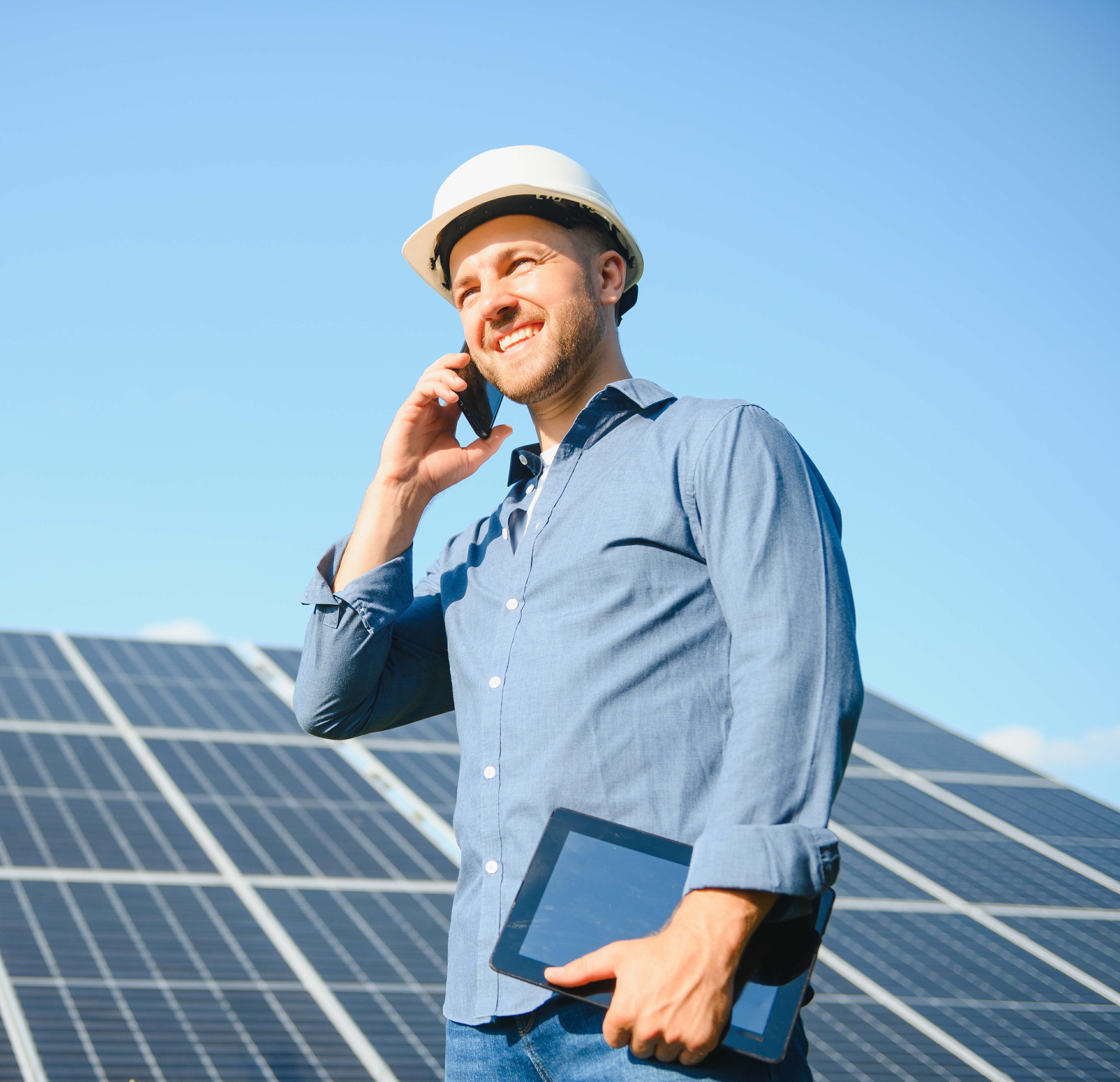 Handwerker mit Bauhelm telefoniert vor einer Photovoltaik-Anlage